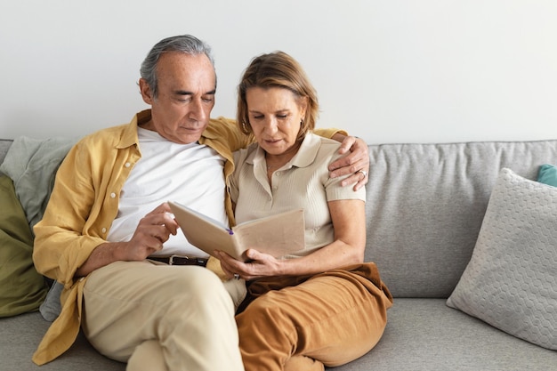 Süße Erinnerungen glückliche ältere verheiratete Ehepartner, die gemeinsam auf dem Sofa sitzen und sich ein Fotoalbum ansehen