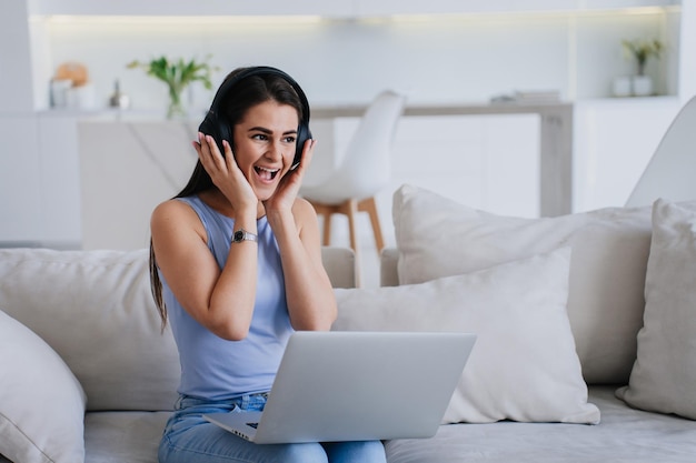 Foto süße, erstaunte hispanische junge frau mit dunklen, lockeren haaren in legerer kleidung arbeitet zu hause auf dem sofa sitzend