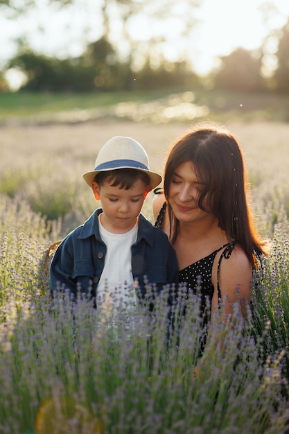 Süße Frau, die ihrem kleinen Sohn Lavendel auf dem Feld zeigt, während sie bei Sonnenuntergang spazieren geht
