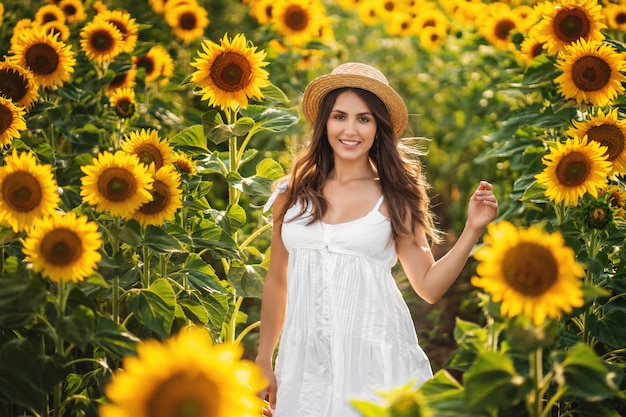 Süße Frau in einem weißen Kleid, das auf einem Feld von Sonnenblumen geht