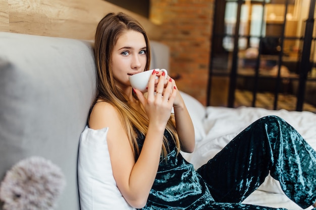 Süße Frau mit Tasse Kaffee auf dem Bett liegend und Latte trinken