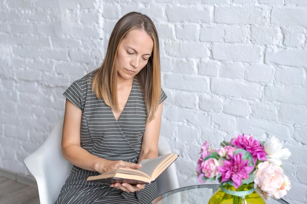 Foto süße frau sitzt in einem sessel am tisch mit buch in der hand liest in grau