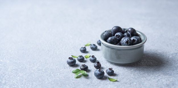 Süße frische Blaubeeren in einer Schüssel auf blauem Betonhintergrund. Makro und Nahaufnahme. Vorderansicht und Platzbild kopieren