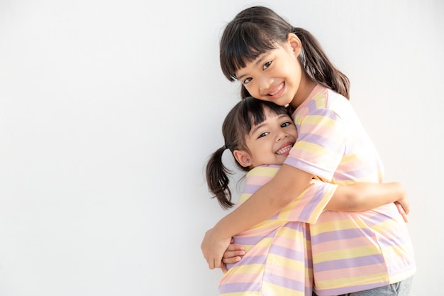 Süße glückliche asiatische Geschwister, die sich umarmen und kuscheln, fühlen Liebe und Verbindung, lächelnde Kindermädchenschwester, die kleine Mädchenschwester auf weißem Hintergrund umarmt, 2 Kinder gute Beziehungen