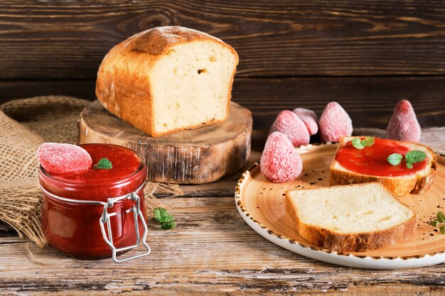 Süße hausgemachte Erdbeermarmelade in einem Glas, selektiver Fokus. Milchbrot, Toast mit Erdbeermarmelade auf einem Holzbrett, Nahaufnahme. Frühstücksidee.