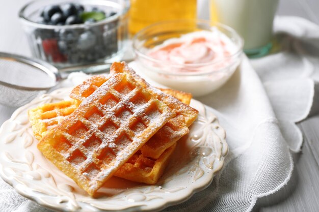 Süße hausgemachte Waffeln auf Teller auf farbigem Holzhintergrund