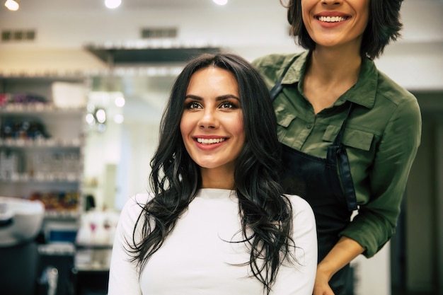 Süße hübsche junge Frau mit ausgefallener Frisur und perfektem Make-up, die in einem Schönheitssalon in den Spiegel schaut.