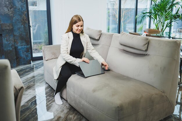 Foto süße junge freiberuflerin in freizeitkleidung, die sich auf dem sofa entspannt, während sie über netbook im internet arbeitet, während sie zu hause an einem projekt arbeitet