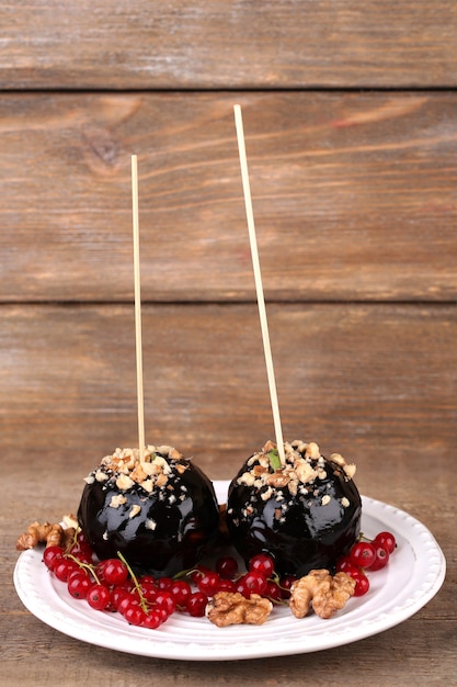 Süße Karamelläpfel auf Stöcken mit Beeren, auf Holztisch