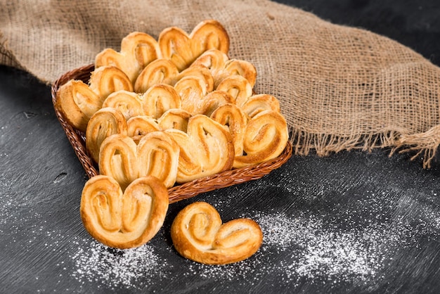 Süße Kekse im Korb auf schwarzem Holzhintergrund