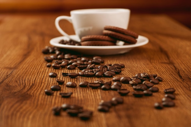 Süße Kekse mit einer Tasse KaffeeFrische Kaffeebohnen auf Holzhintergrund