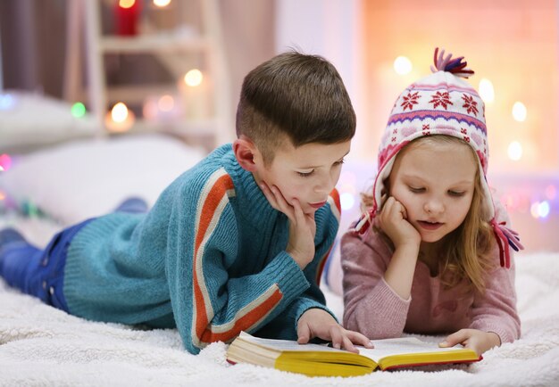 Süße Kinder lesen Buch auf dem Boden im dekorierten Weihnachtszimmer