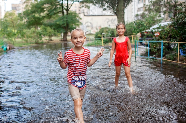 Süße Kinder springen und schwimmen in den Pfützen nach warmem Sommerregen glückliche Kindheit happy