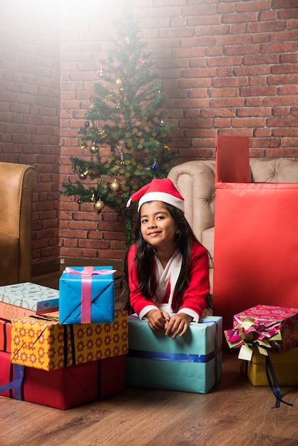 Süße kleine indische asiatische Kinder feiern Weihnachten zu Hause mit Weihnachtsmütze, Geschenken und Weihnachtsbaum