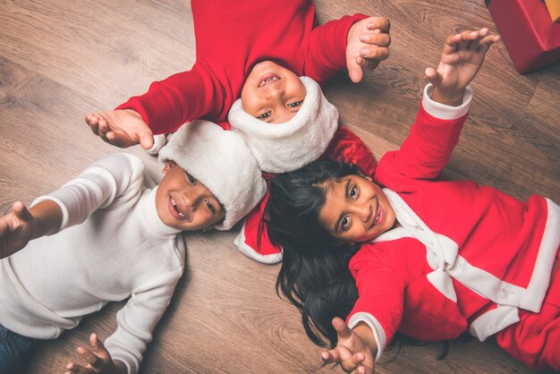 Süße kleine indische asiatische Kinder feiern Weihnachten zu Hause mit Weihnachtsmütze, Geschenken und Weihnachtsbaum