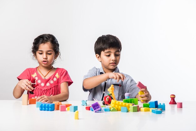 Süße kleine indische asiatische Kinder spielen mit bunten Plastikspielzeug oder Blöcken beim Sitzen am Tisch oder isoliert auf weißem Hintergrund