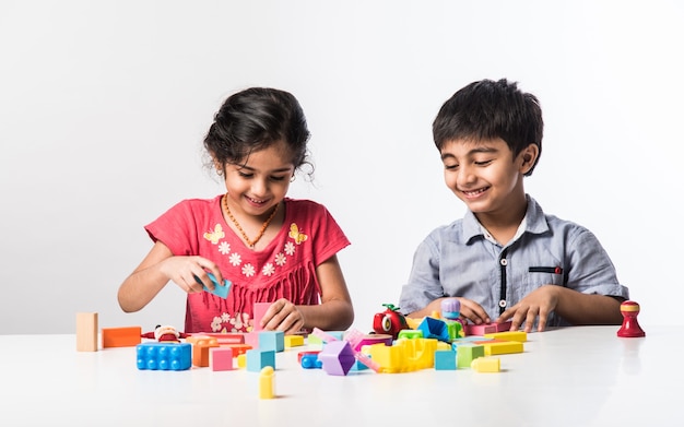 Süße kleine indische asiatische Kinder spielen mit bunten Plastikspielzeug oder Blöcken beim Sitzen am Tisch oder isoliert auf weißem Hintergrund