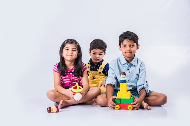 Süße kleine indische oder asiatische Kinder spielen mit Spielzeug oder Blöcken und haben Spaß beim Sitzen am Tisch oder isoliert auf weißem Hintergrund white