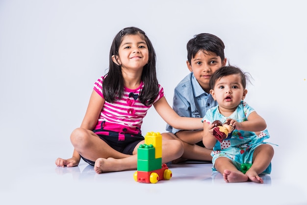 Süße kleine indische oder asiatische Kinder spielen mit Spielzeug oder Blöcken und haben Spaß beim Sitzen am Tisch oder isoliert auf weißem Hintergrund white