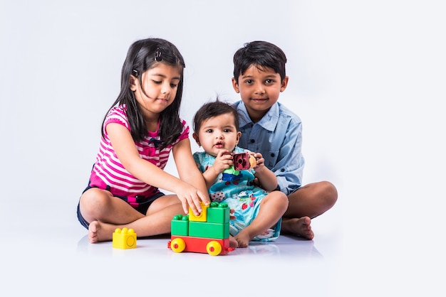 Süße kleine indische oder asiatische Kinder spielen mit Spielzeug oder Blöcken und haben Spaß beim Sitzen am Tisch oder isoliert auf weißem Hintergrund white