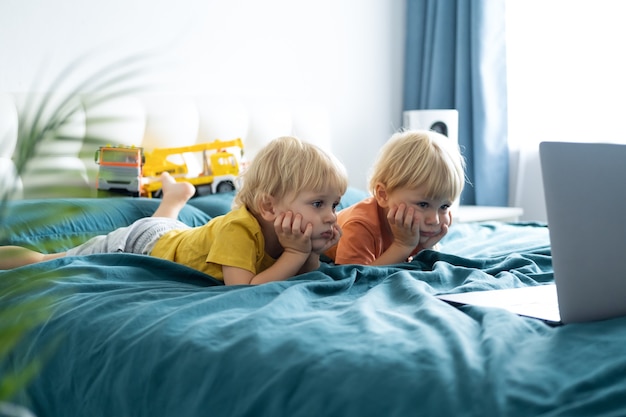 Süße kleine kaukasische Kinderjungen Zwillinge mit Laptop im Bett zu Hause. Kinder, die Technologie verwenden.