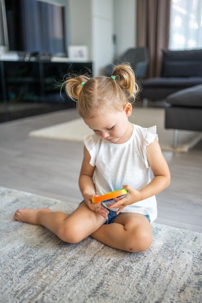 Süße kleine Mädchen, die mit Begeisterung spielen, knallen es, sensorisches Spielzeug, Kreisform. Kleines Weibchen drückt zu Hause bunte, regenbogenfarbene, matschige, weiche Silikonblasen