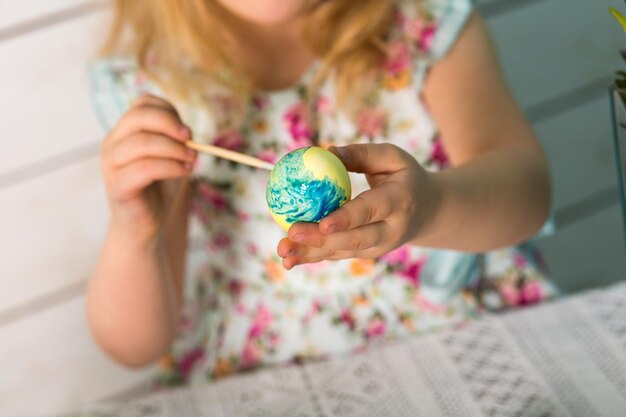 Süße kleine Mädchenblondine malt farbige Ostereier mit einer Quaste. Thema Ostern