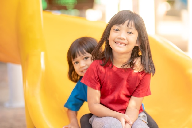 süße kleine Mädchengeschwister, die sich an einem sonnigen Sommertag auf dem Spielplatz im Freien amüsieren