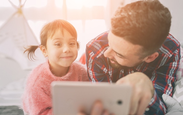 Süße kleine Tochter und ihr hübscher junger Vater spielen zusammen im Kinderzimmer. Papa und Kind verbringen Zeit zusammen, während sie im Schlafzimmer auf dem Boden sitzen.