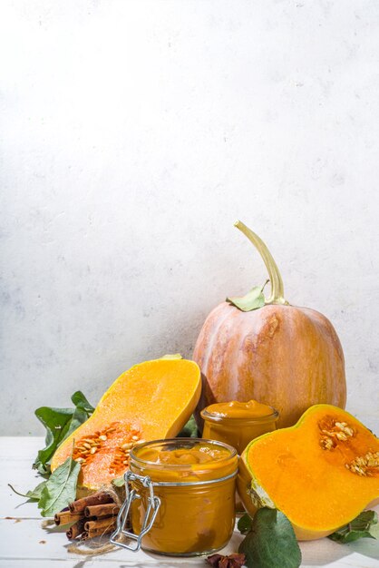 Süße Kürbiskuchenmarmelade. Hausgemachte Konfitüre mit Kürbispüree und traditionellen Herbstgewürzen. Zimt, Anis. Mit frischem Butternut-Kürbis und Herbstlaub auf weißem Holzhintergrund