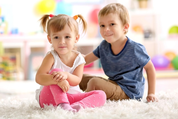 Süße lustige Kinder spielen, während sie zu Hause auf dem Teppich sitzen