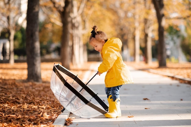 Süße Mädchen im Alter von 2-3 Jahren tragen gelbe Regenjacke und Stiefel halten Regenschirm im Herbstpark im Freien