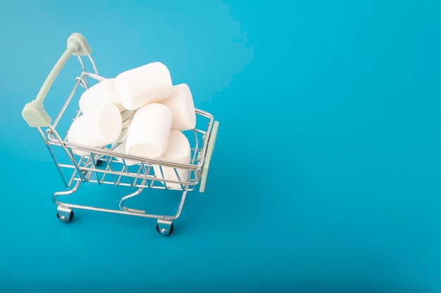 Süße Marshmallow-Bonbons in einem Einkaufswagen auf blauem Hintergrund mit Kopierraum