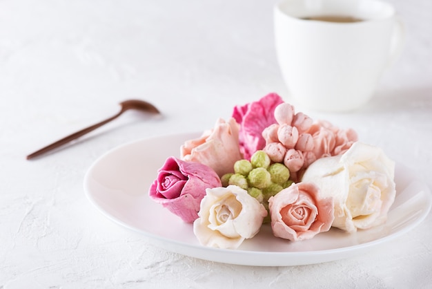 Süße Rosen aus Marshmallows auf einem Teller mit einer Tasse grünem Tee.