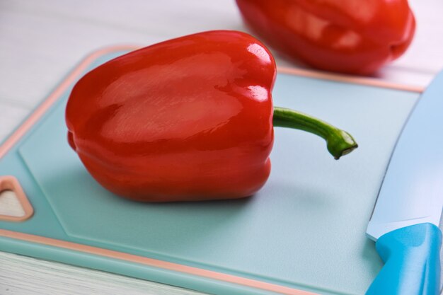 Süße rote Paprika und ein Messer auf einem Schneidebrett auf einer weißen Holzoberfläche