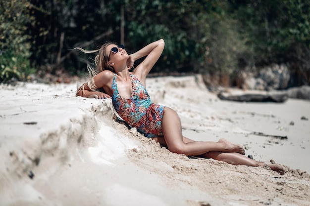 Süße schlanke Frau in Sonnenbrille und Badeanzug am weißen Strand gegen die Bäume, Arm im Haer; Sonnenkonzept.