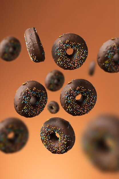 Süße Schokoladenkrapfen mit bunten Zuckerstreuseln auf orangefarbenem Hintergrund. Dessert in Bewegung und Schweben