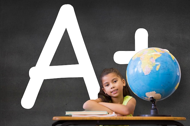 Süße Schüler sitzen am Schreibtisch an der schwarzen Wand mit einer Plusnote