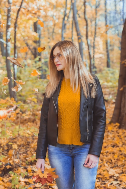 Süße Smiley-Frau mit Herbstlaub im saisonalen Lifestyle- und Freizeitkonzept des Herbstparks