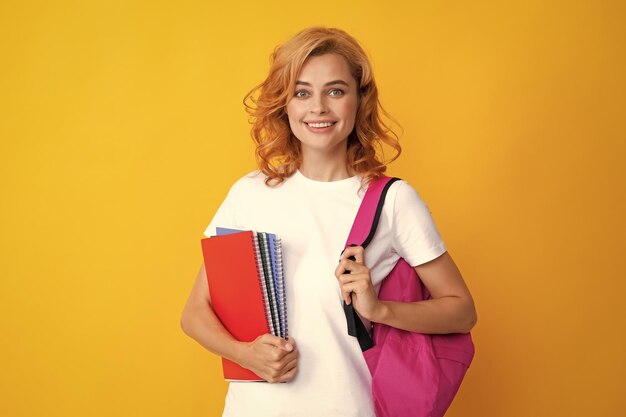 Süße Studentin mit Rucksack hält einige Dokumente und Bücher über gelbem Hintergrund Porträt