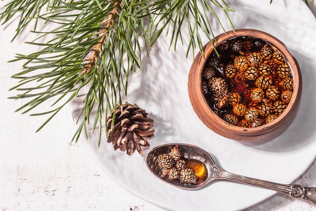 Süße Tannenzapfenmarmelade. Traditionelles sibirisches Dessert, frische immergrüne Zweige. Trendiges hartes Licht, dunkler Schatten. Weißer Holzhintergrund, Ansicht von oben