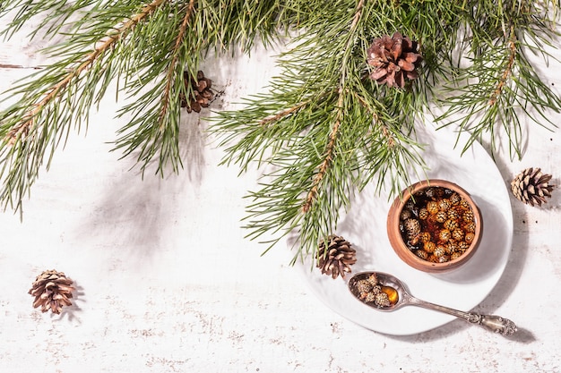 Süße Tannenzapfenmarmelade. Traditionelles sibirisches Dessert, frische immergrüne Zweige. Trendiges hartes Licht, dunkler Schatten. Weißer Holzhintergrund, Ansicht von oben