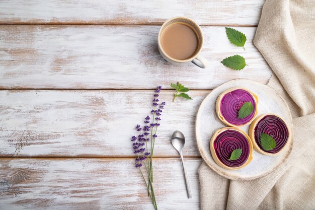 Süße Törtchen mit Gelee und Milchcreme mit einer Tasse Kaffee auf einem weißen Holz