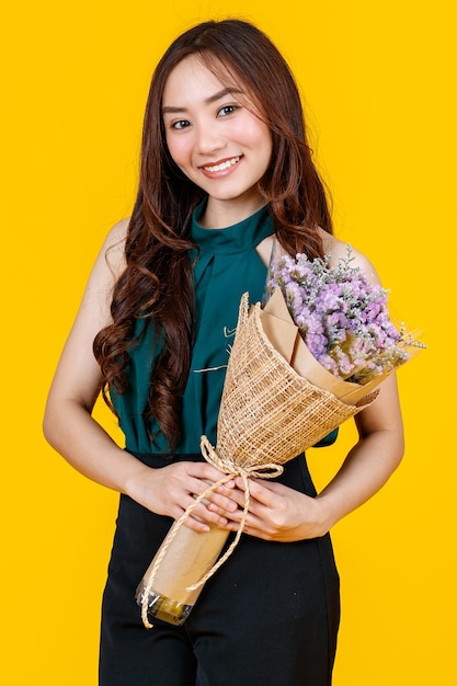 Süße und hübsche lockige Haare Asiatische Brünette mit Blumenstrauß mit fröhlichem und fröhlichem, Studioaufnahme einzeln auf hellgelbem Hintergrund.