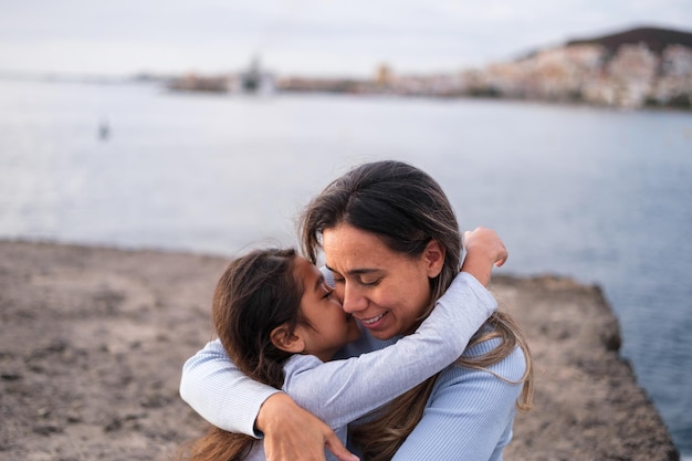 Süße und zärtliche Umarmung von Mutter und Tochter bei einem Spaziergang am Meer bei Sonnenuntergang Konzept Lifestyle Mutterschaft Zärtlichkeit