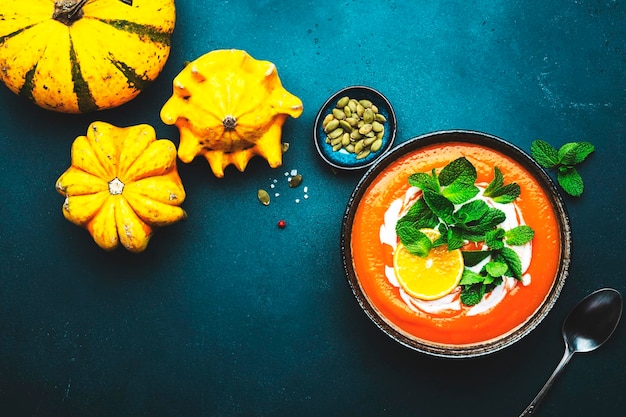 Süße vegane Kürbissuppe mit Kokoscreme, Orange und Minze Gesunde vegetarische Hausmannskost im Winter oder Herbst Suppenschüssel auf grünem Tischhintergrund Ansicht von oben