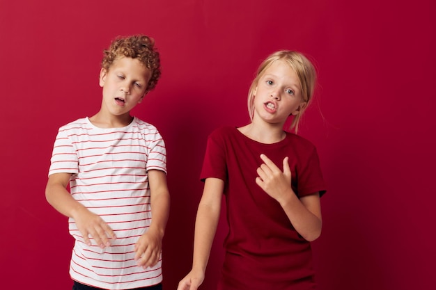 Süße Vorschulkinder lächeln und posieren in Freizeitkleidung vor rotem Hintergrund