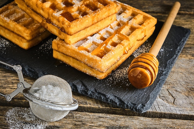 Süße Waffeln mit Honig beträufelt und mit Puderzucker auf einer Schiefertafel bestreut