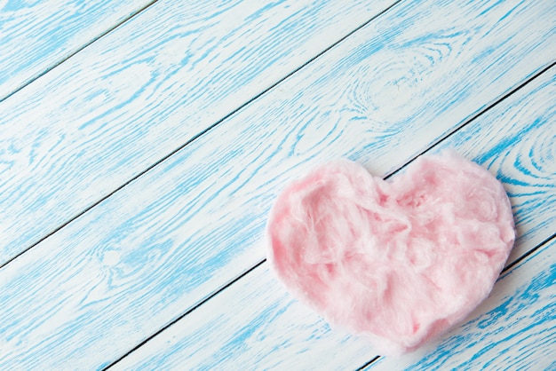 Süße zuckerwatte in herzform auf blauem holztisch. speicherplatz kopieren