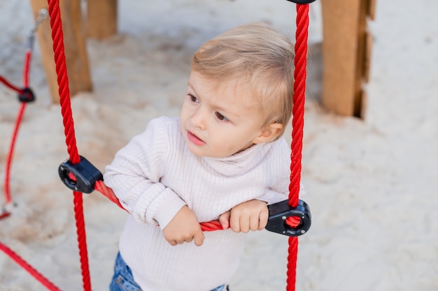 süßer blonder Junge, der draußen auf einer Strickleiter spielt